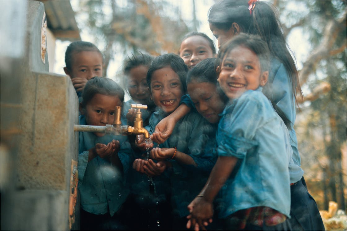 Photo of a group of 8 smiling kids reaching out to feel the clean water flowing out of a well.